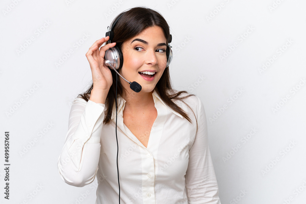 Telemarketer caucasian woman working with a headset isolated on white background listening to something by putting hand on the ear Telemarketer caucasian woman working with a headset isolated on white background listening to something by putting hand on the ear