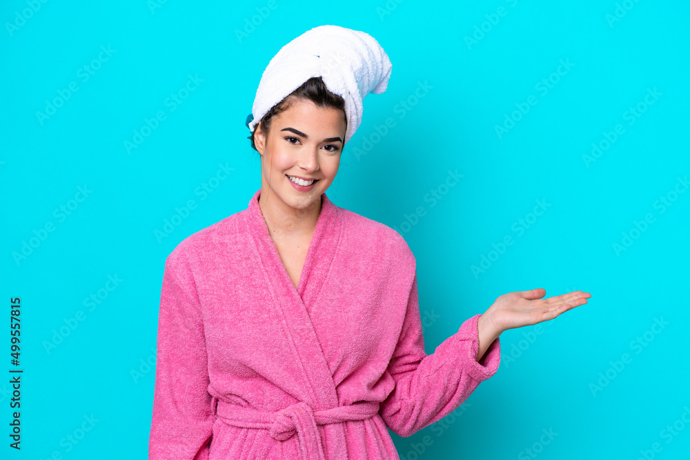 Young Brazilian woman with a bathrobe isolated on blue background presenting an idea while looking smiling towards Young Brazilian woman with a bathrobe isolated on blue background presenting an idea while looking smiling towards