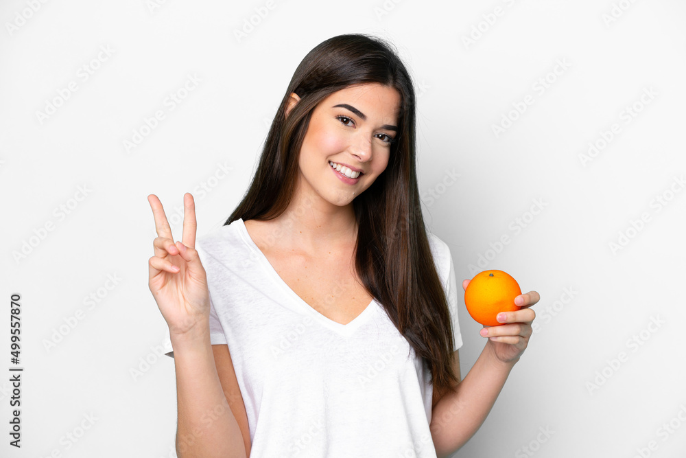 Young Brazilian woman holding an orange isolated on white background smiling and showing victory sign Young Brazilian woman holding an orange isolated on white background smiling and showing victory sign