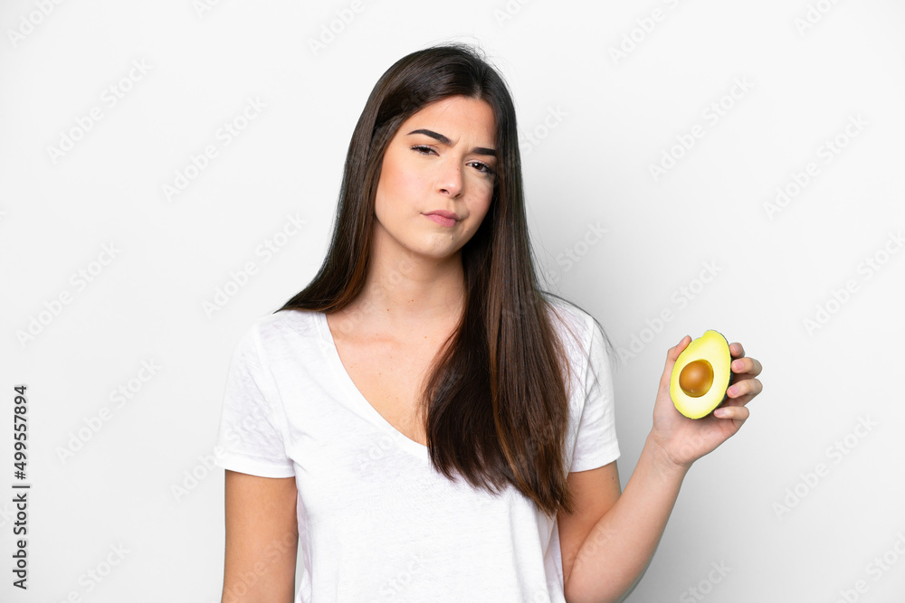 Young Brazilian woman holding an avocado isolated on white background with sad expression Young Brazilian woman holding an avocado isolated on white background with sad expression