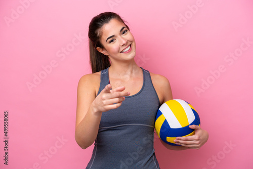 Young Brazilian woman playing volleyball isolated on pink background pointing front with happy expression