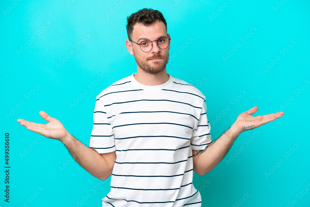 Young Brazilian man isolated on blue background having doubts Young Brazilian man isolated on blue background having doubts