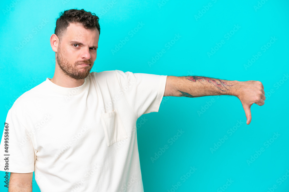 Young Brazilian man isolated on blue background showing thumb down with negative expression Young Brazilian man isolated on blue background showing thumb down with negative expression