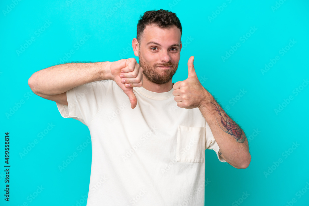Young Brazilian man isolated on blue background making good-bad sign. Undecided between yes or not Young Brazilian man isolated on blue background making good-bad sign. Undecided between yes or not