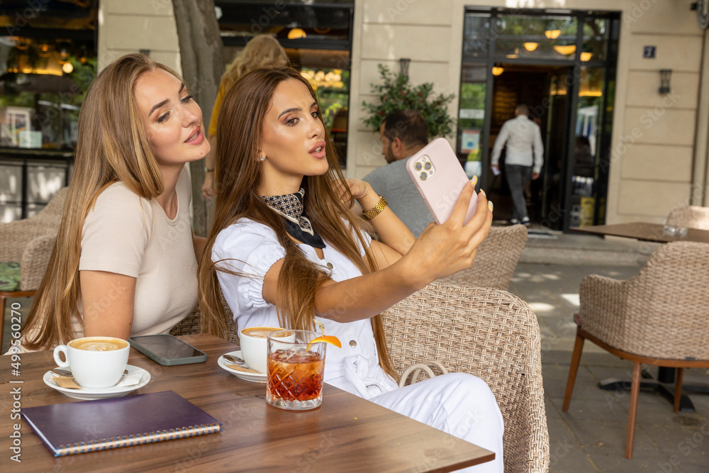Two girlfriends taking selfie in a cafe bar outside
