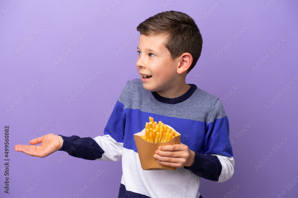 Little boy holding fried chips isolated on purple background with surprise expression while looking side Little boy holding fried chips isolated on purple background with surprise expression while looking side