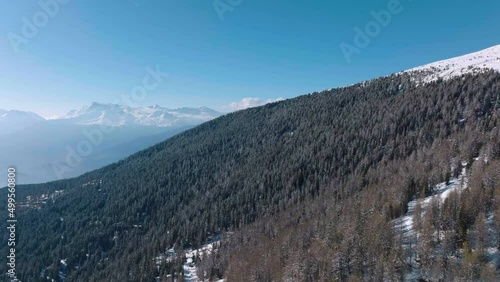 Snowy Forests Of Larch And La Louere Hamlet On The Slopes Of Mont Noble Summit, Rhone Valley In Val d’Herens Valais Of Switzerland-  Aerial Overflying Shot photo