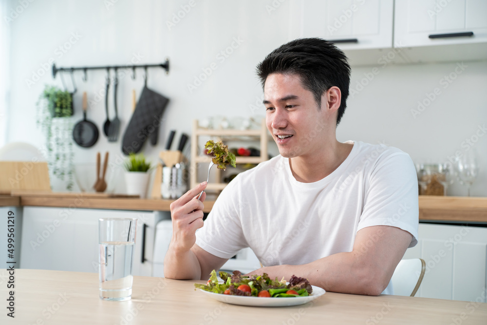 Asian attractive handsome male eating green salad in kitchen at home. Asian attractive handsome male eating green salad in kitchen at home.