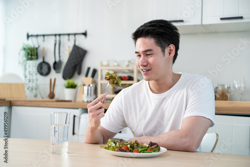 Asian attractive handsome male eating green salad in kitchen at home. 