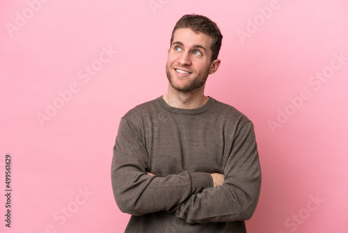 Young caucasian man isolated on pink background looking up while smiling