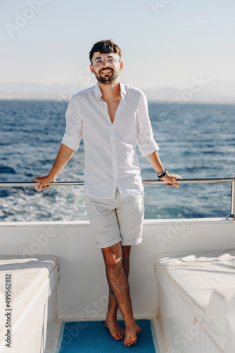 A stylish, young smiling happy man on the deck of a cruise ship on a sunny day and blue sky, looks into the camera. The concept of sea travel and recreation