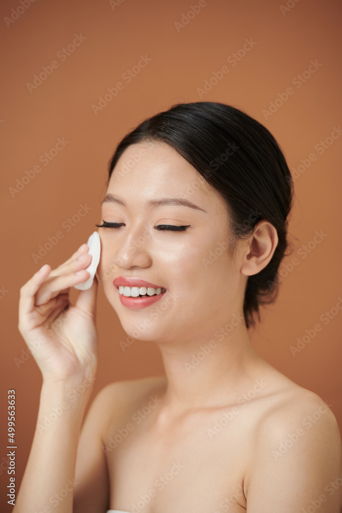 Smiling young woman wipingface with cotton pad with moisturizing toner Smiling young woman wipingface with cotton pad with moisturizing toner