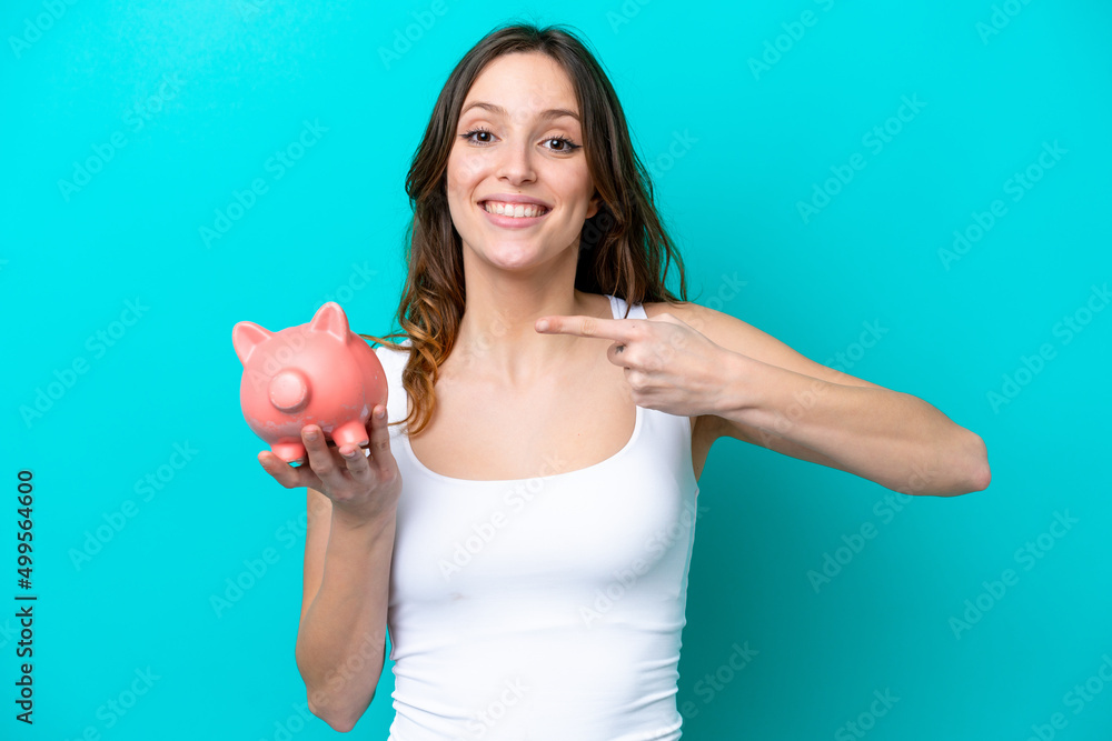 Young Caucasian woman holding a piggybank isolated on blue bakcground with surprise facial expression Young Caucasian woman holding a piggybank isolated on blue bakcground with surprise facial expression