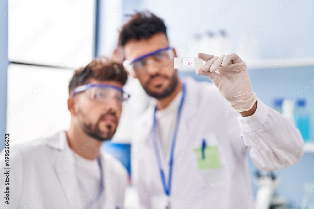 Young couple wearing scientist uniform holding sample at laboratory Young couple wearing scientist uniform holding sample at laboratory