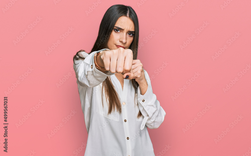 Young beautiful woman wearing casual white shirt punching fist to fight, aggressive and angry attack, threat and violence Young beautiful woman wearing casual white shirt punching fist to fight, aggressive and angry attack, threat and violence