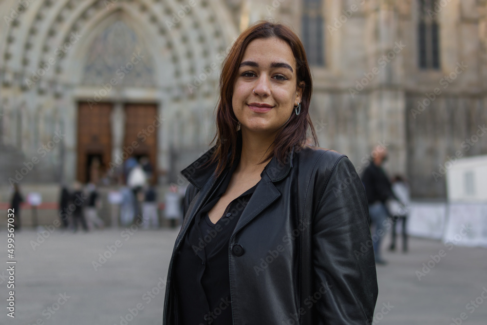 Headshot image of a lovely hispanic girl dressed with black clothes who is standing on a street of Barcelona with a church behind her Headshot image of a lovely hispanic girl dressed with black clothes who is standing on a street of Barcelona with a church behind her