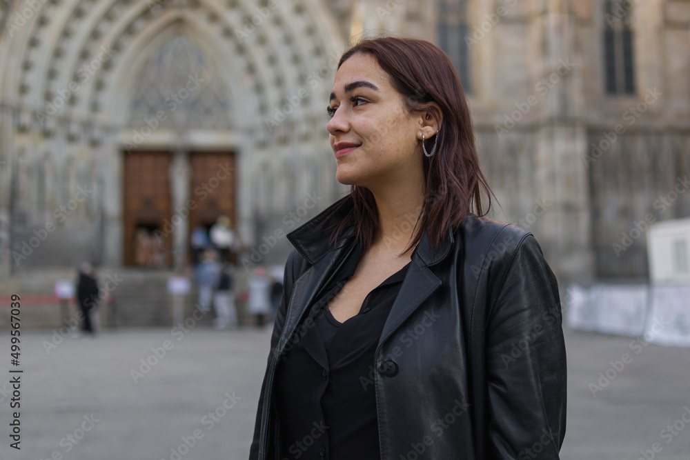 Fototapeta premium headshot portrait with copy space of a likable latin woman dressed with black clothes who is standing on a street of Barcelona where there is a church that is behind her