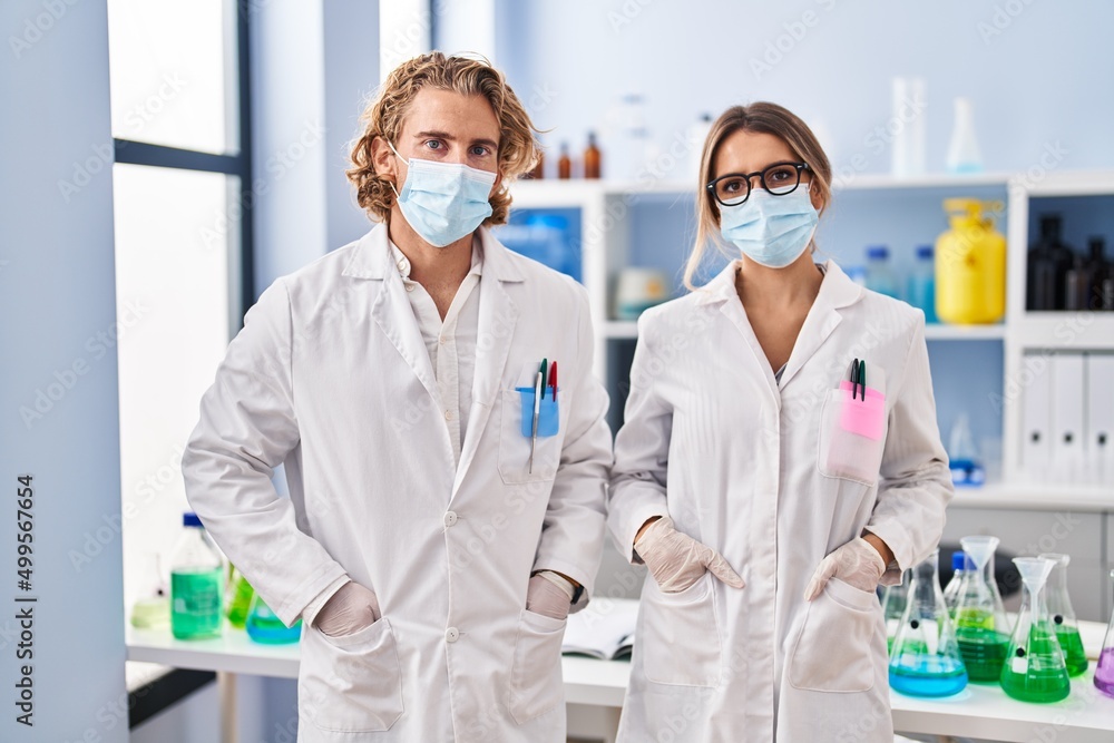 Man and woman wearing scientist uniform and medical mask at laboratory Man and woman wearing scientist uniform and medical mask at laboratory