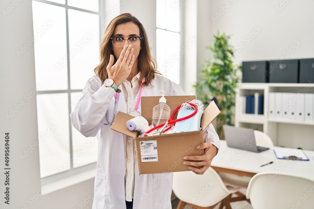 Young doctor woman holding box with medical items covering mouth with hand, shocked and afraid for mistake. surprised expression Young doctor woman holding box with medical items covering mouth with hand, shocked and afraid for mistake. surprised expression