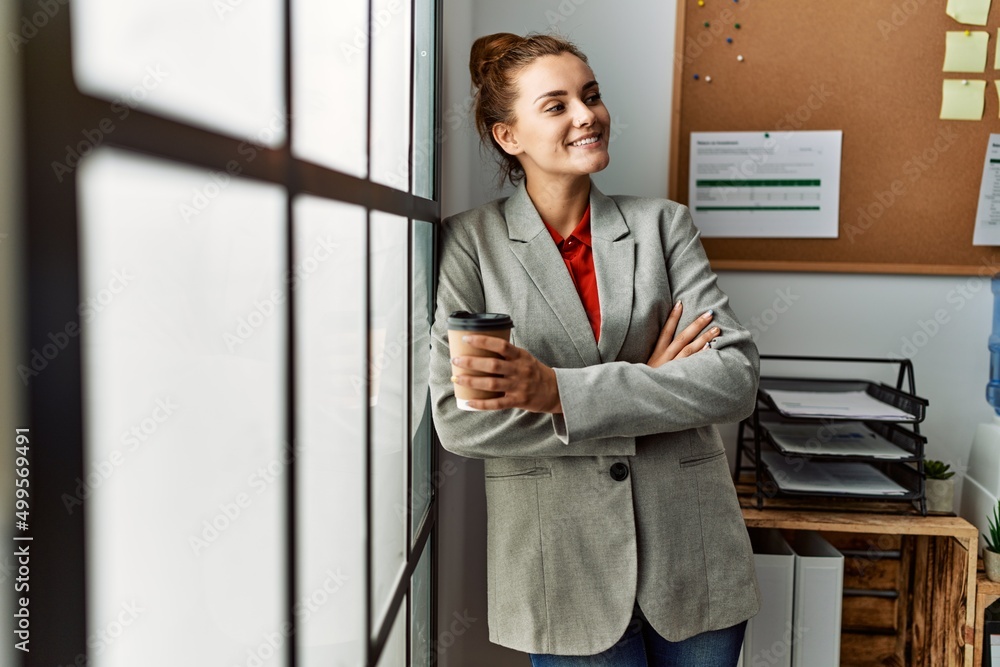 Young woman business worker drinking coffee standing with arms crossed gesture at office Young woman business worker drinking coffee standing with arms crossed gesture at office