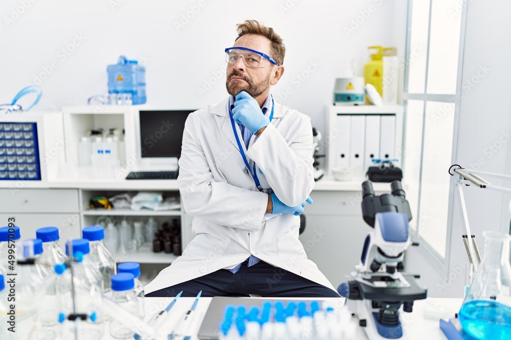 Middle age man working at scientist laboratory serious face thinking about question with hand on chin, thoughtful about confusing idea Middle age man working at scientist laboratory serious face thinking about question with hand on chin, thoughtful about confusing idea