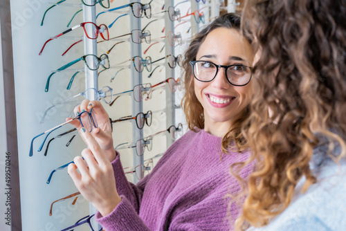 Two happy female friends in a optic shop wearing glasses while choosing some new pair of glasses