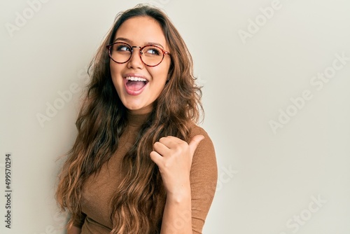 Wallpaper Mural Young hispanic girl wearing casual clothes and glasses smiling with happy face looking and pointing to the side with thumb up. Torontodigital.ca