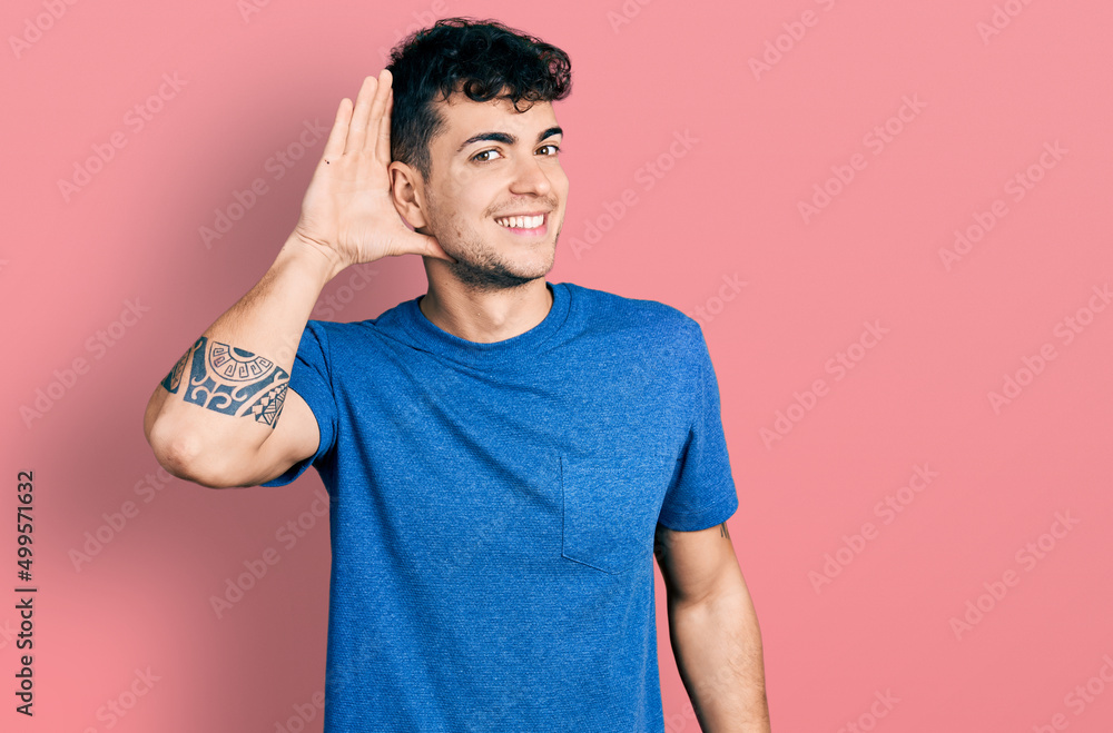 Young hispanic man wearing casual t shirt smiling with hand over ear listening an hearing to rumor or gossip. deafness concept. Young hispanic man wearing casual t shirt smiling with hand over ear listening an hearing to rumor or gossip. deafness concept.