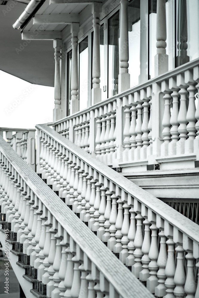 Obraz premium White staircase with balusters. Bright building with a beautiful staircase. Repetitive elements in architecture. Marble staircase in the restaurant
