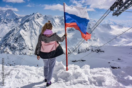 Young girl on the background of snow-capped mountains and the flag of Russia. Elbrus April 25, 2019