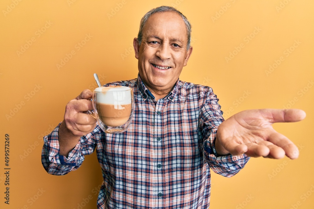 Handsome senior man with grey hair drinking a cup coffee smiling cheerful offering palm hand giving assistance and acceptance. Handsome senior man with grey hair drinking a cup coffee smiling cheerful offering palm hand giving assistance and acceptance.
