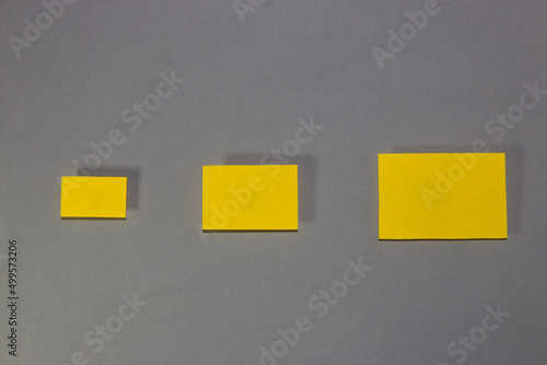 three (3) blank yellow papers of different sizes from smallest to largest arranged side by side, in a row, from left to right from smallest to largest