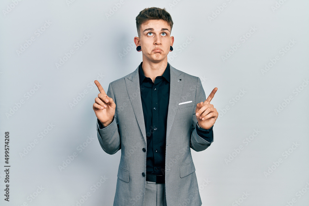 Young caucasian boy with ears dilation wearing business jacket pointing up looking sad and upset, indicating direction with fingers, unhappy and depressed. Young caucasian boy with ears dilation wearing business jacket pointing up looking sad and upset, indicating direction with fingers, unhappy and depressed.