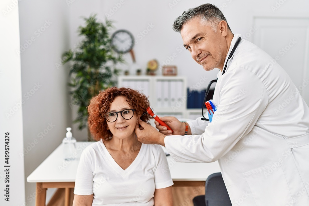 Obraz premium Middle age man and woman wearing doctor uniform examining ear having medical consultation at clinic