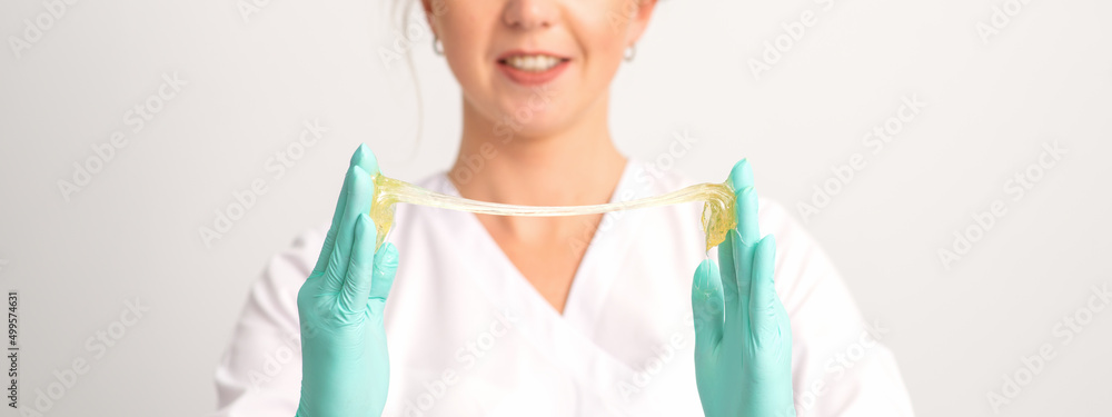 Young caucasian smiling female beautician holding wax for depilation over white background. Yellow sugar paste in hands master of depilation. Epilation concept Young caucasian smiling female beautician holding wax for depilation over white background. Yellow sugar paste in hands master of depilation. Epilation concept