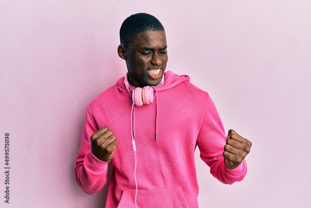 Young african american man wearing gym clothes and using headphones excited for success with arms raised and eyes closed celebrating victory smiling. winner concept. Young african american man wearing gym clothes and using headphones excited for success with arms raised and eyes closed celebrating victory smiling. winner concept.