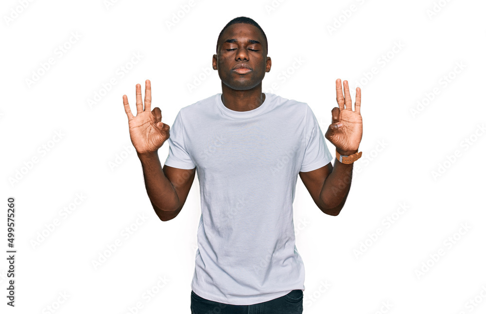 Young african american man wearing casual white t shirt relaxed and smiling with eyes closed doing meditation gesture with fingers. yoga concept. Young african american man wearing casual white t shirt relaxed and smiling with eyes closed doing meditation gesture with fingers. yoga concept.