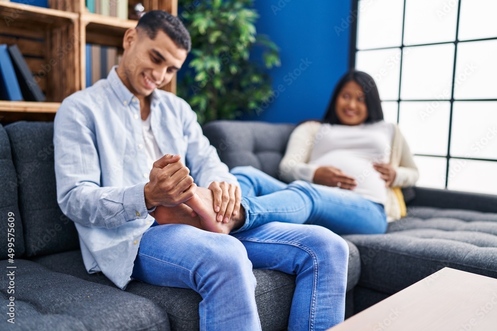 Young latin couple expecting baby massaging foot at home Young latin couple expecting baby massaging foot at home