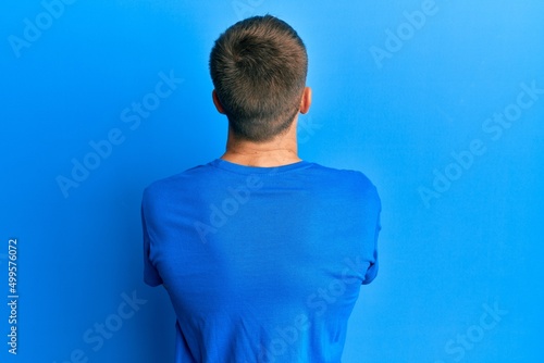 Young caucasian man wearing casual blue t shirt standing backwards looking away with crossed arms photo