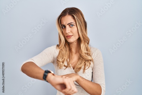 Young blonde woman standing over isolated background in hurry pointing to watch time, impatience, upset and angry for deadline delay