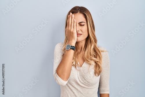 Young blonde woman standing over isolated background yawning tired covering half face, eye and mouth with hand. face hurts in pain.