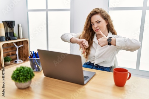 Young caucasian woman working at the office using computer laptop doing thumbs up and down, disagreement and agreement expression. crazy conflict