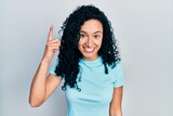 Young hispanic woman with curly hair wearing casual blue t shirt pointing finger up with successful idea. exited and happy. number one.