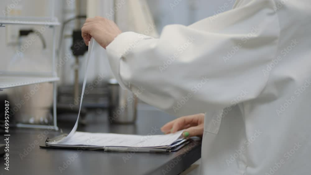 White coat female scientist in lab reading through research notes on a clipboard White coat female scientist in lab reading through research notes on a clipboard
