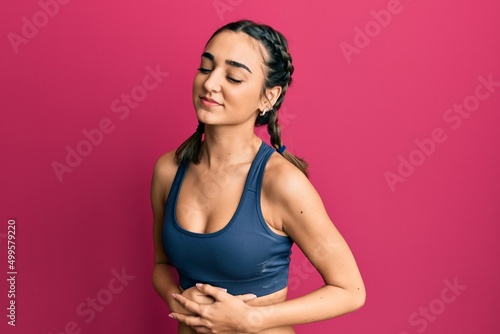 Young brunette girl wearing sportswear and braids with hand on stomach because nausea, painful disease feeling unwell. ache concept.