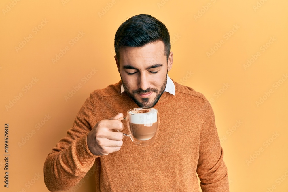 Handsome hispanic man enjoying a cup of coffee over yellow background Handsome hispanic man enjoying a cup of coffee over yellow background