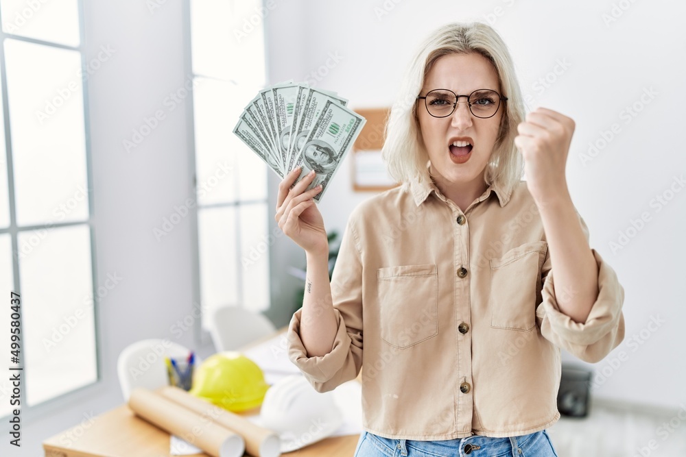 Young beautiful caucasian woman at construction office holding money annoyed and frustrated shouting with anger, yelling crazy with anger and hand raised Young beautiful caucasian woman at construction office holding money annoyed and frustrated shouting with anger, yelling crazy with anger and hand raised