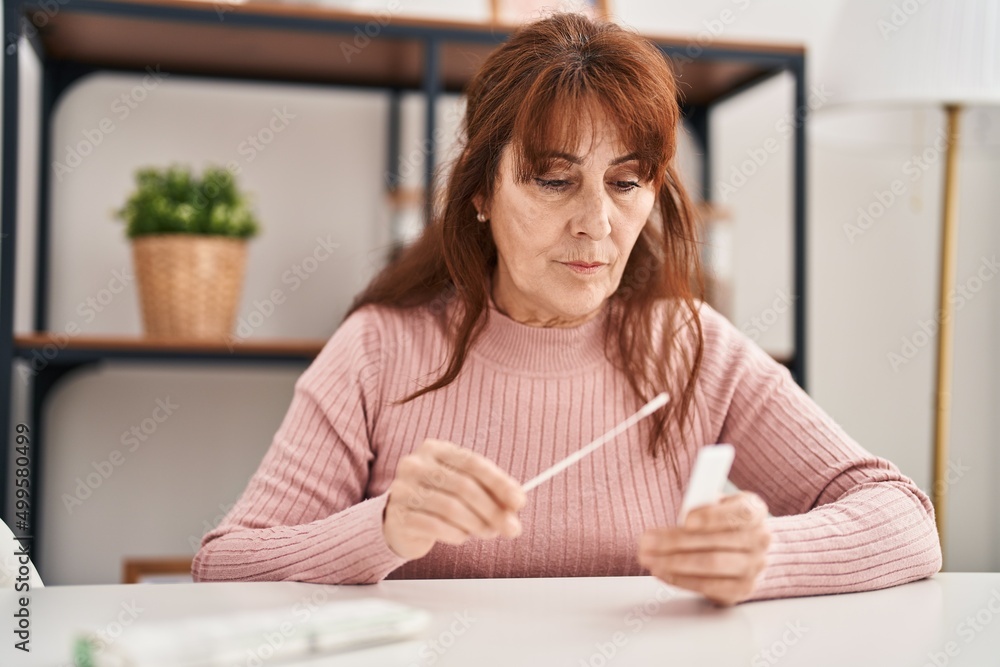 Middle age woman holding antigen covid-19 test sitting on table at home Middle age woman holding antigen covid-19 test sitting on table at home