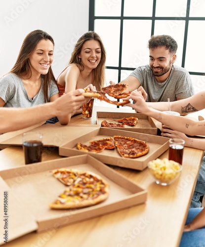 Group of young people smiling happy eating italian pizza sitting on the table at home