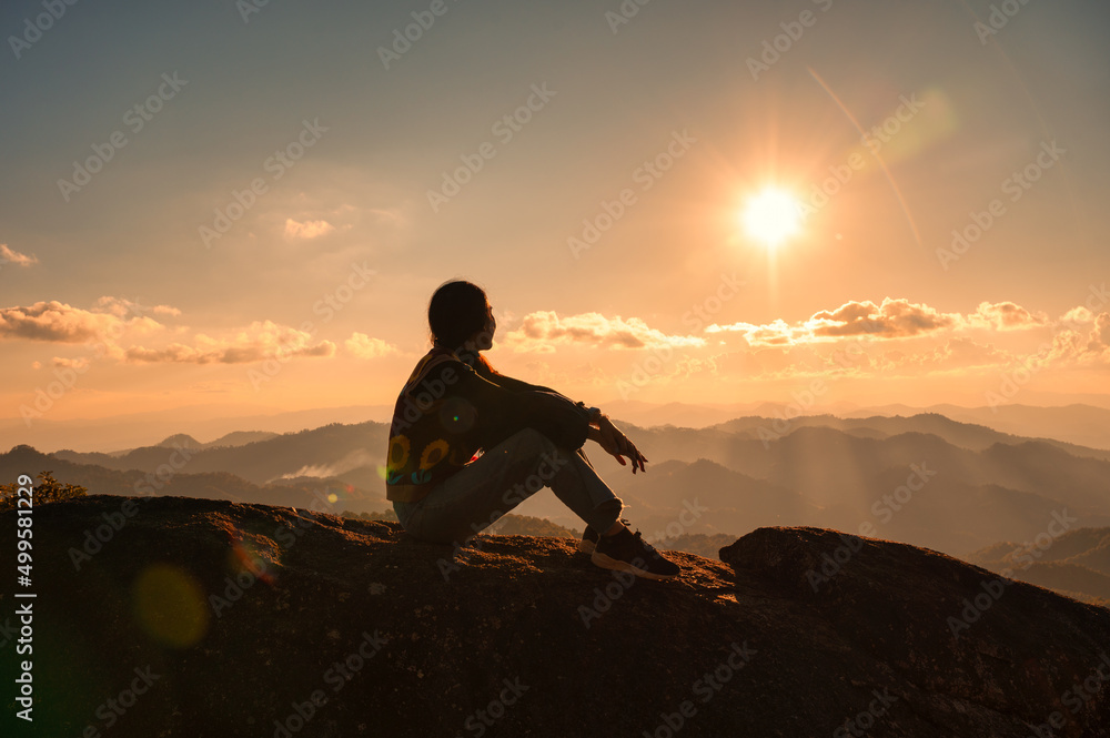 Silhouette young hiker woman relaxing and enjoying the sunset view on top of mountain peak at national park